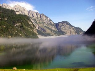 Nebelschleier über klaren Bergsee, darüber Felsgebirge