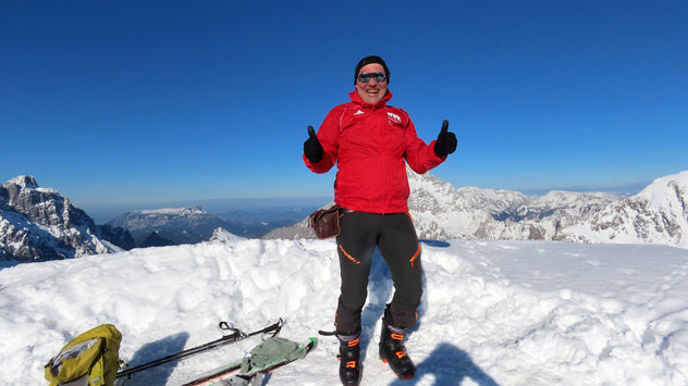 Skibergsteiger freut sich über den Gipfelerfolg an einem sonnigen Tag mit zwei erhobenen Daumen 
