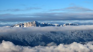 Verschneiter, felsiger Plateauberg ragt über ein breites Wolkenband hinaus