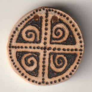 Mit Brennglas und Sonne bebrannte Holzscheibe mit Mutter Erde Symbol mit Spiralen
