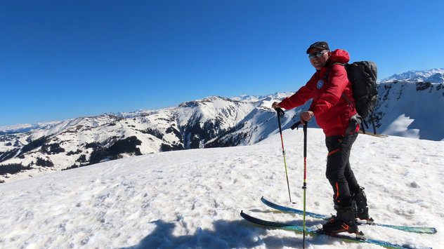 Skitourengeher mit roter Windjacke steht auf einem winterlichen Vorgipfel 