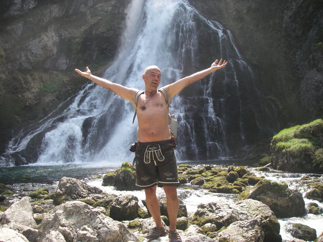 Mann mit ausgebreiteten Armen an einem Wasserfall 
