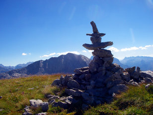 Steinmandl mit Hut auf einem einsamen Berggipfel bei Sonnenschein