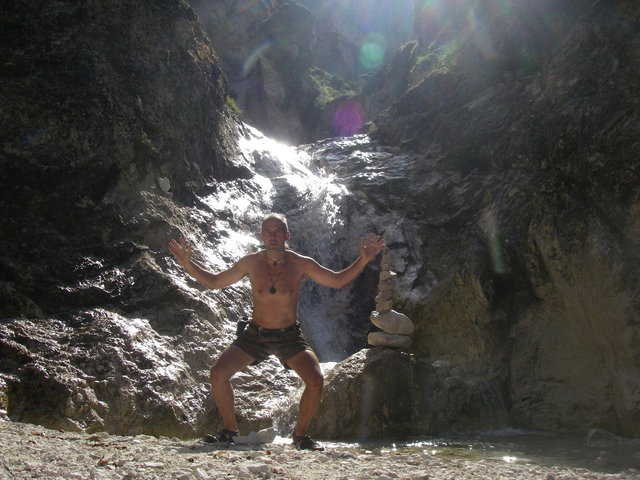 Mann mit nacktem Oberkörper im Sommer an einem wildromantischen Wasserfall in den Bergen