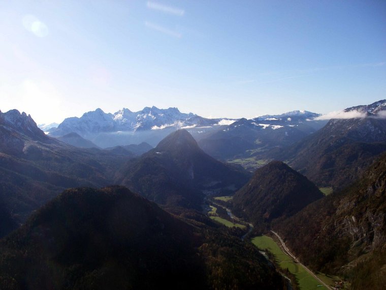 Ausblick von einem Gipfel in ein breites Tal un zu schneebedeckten Bergen