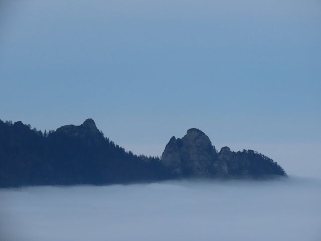 Bergrelief mit Hexengestalt über Wolkenmeer
